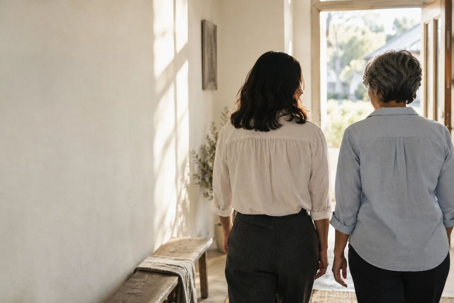 two women walking side by side toward daylight, seen from behind